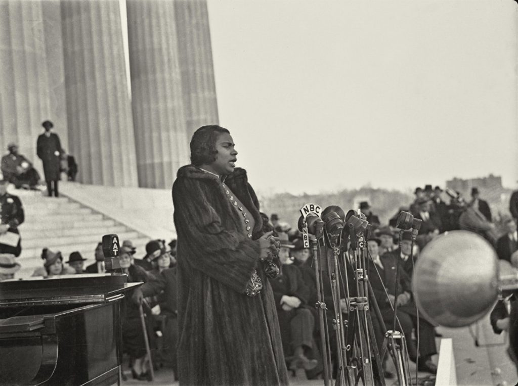 Black and white image of Marian Anderson speaking to an audience with microphones in front of her