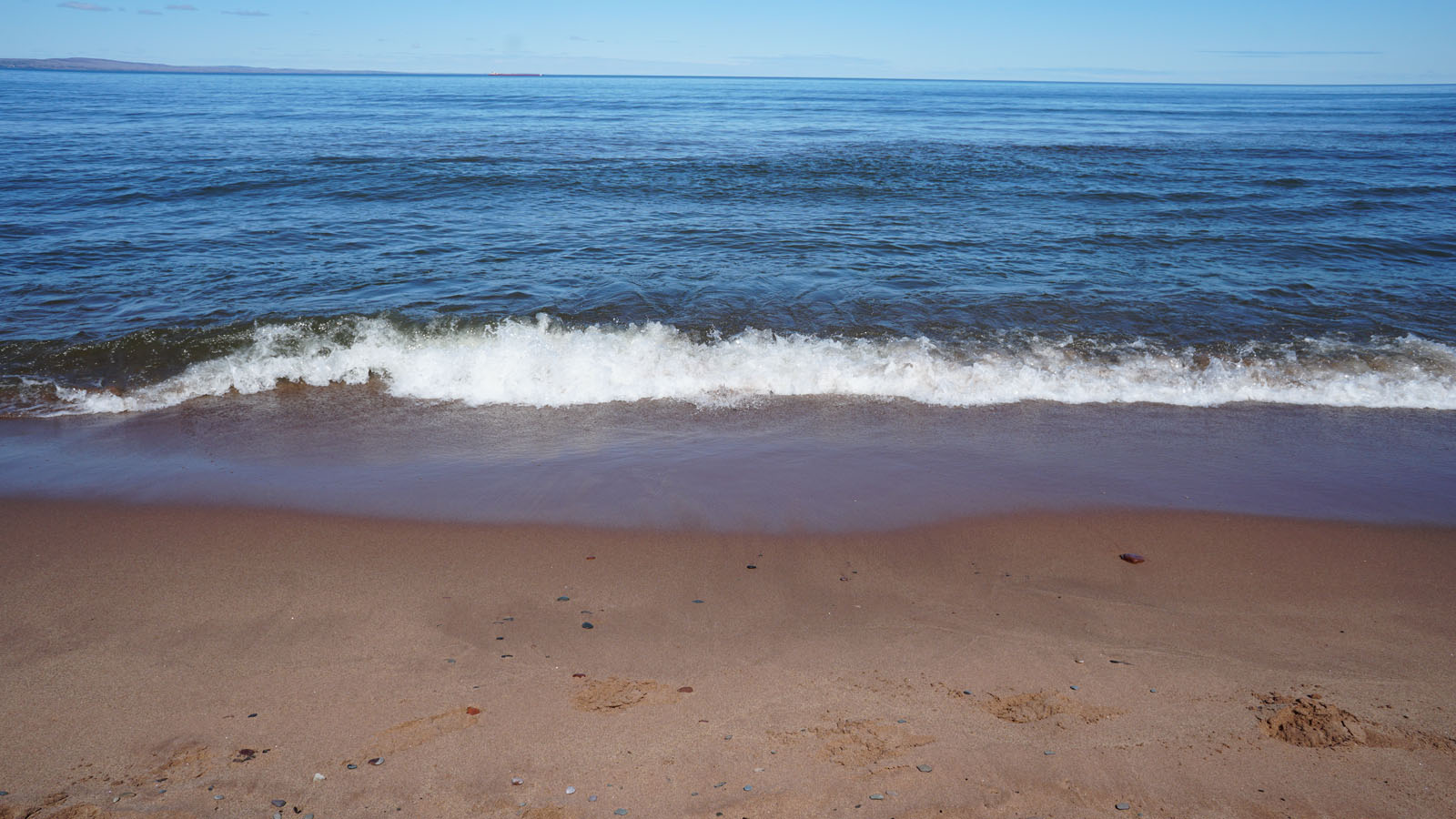 A sandy beach with small waves and ripples coming to shore
