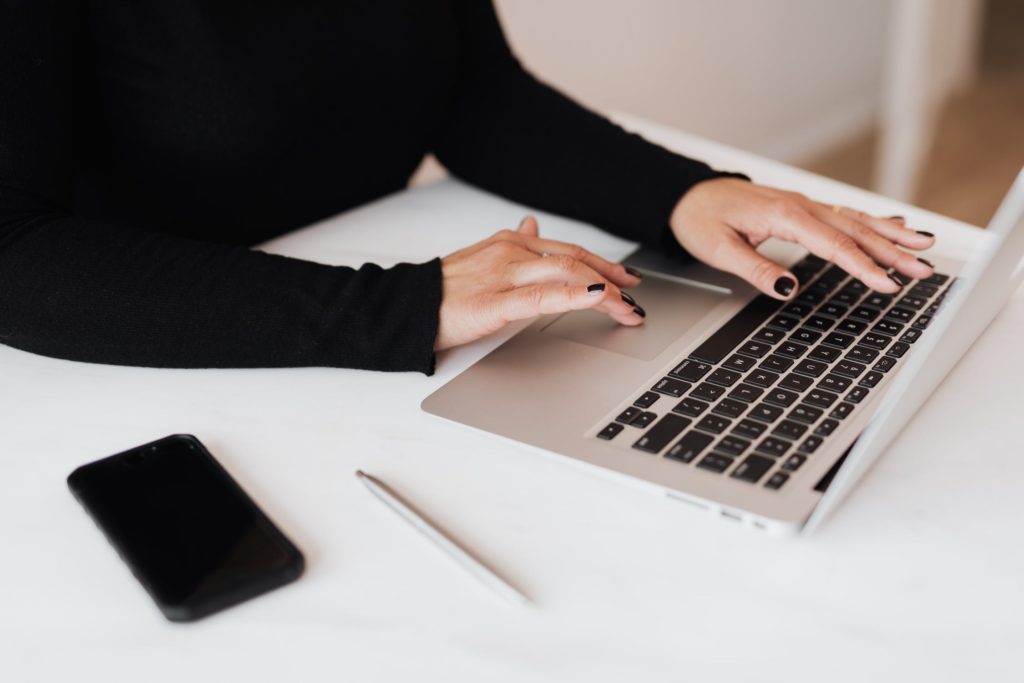 An aerial view of a woman's arms and hands using a laptop computer, with a pen and cellphone beside her